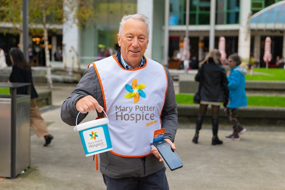 Volunteer wears bib that says mary potter hospice and holds donations bucket and EFTPOS terminal